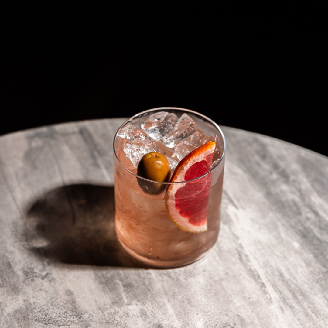 Short glass of Rakija & Tonic garnished with grapefruit and an olive