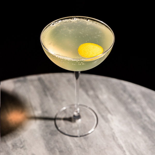 A bright Mediterranean 75 cocktail, a variation of the French 75 using rakija, served in a coupe glass with a lemon twist