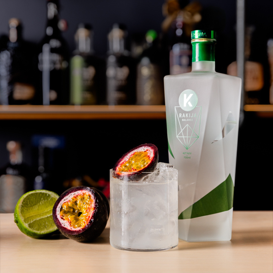 An angular, striking bottle of Kabina Balance Rakija stands next to the Rakija Hardshake cocktail, garnish
