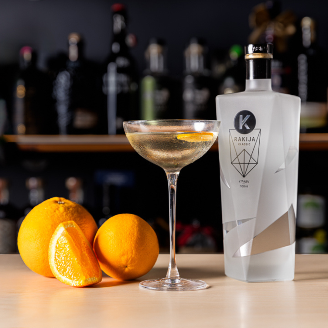 A bottle of Kabina Classic Rakija next to the Black Seas cocktail garnished with orange