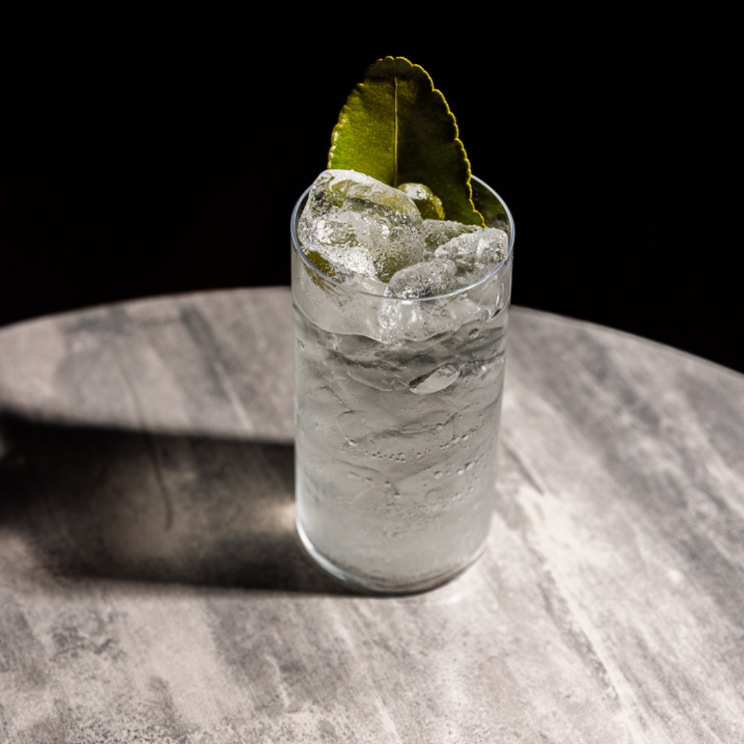 A tall glass of Kabina Rakija and Yuzu Soda over ice, garnished with a lime leaf