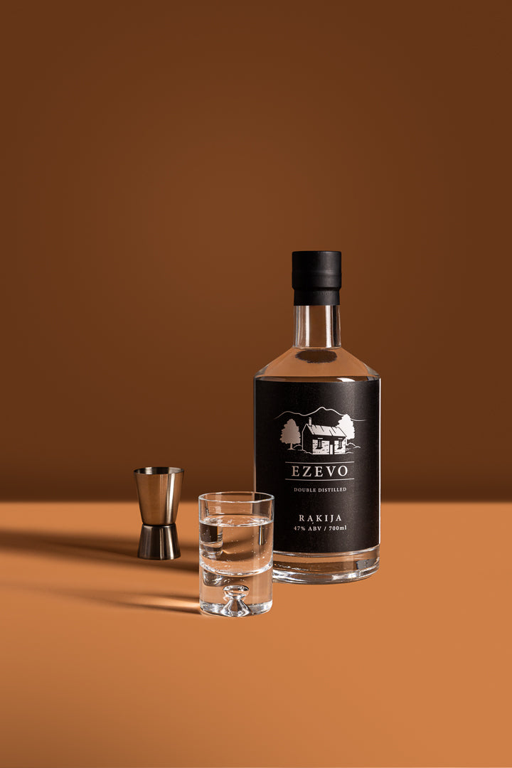 A bottle of Ezevo Classic 47% ABV, styled with a shot glass of rakija.