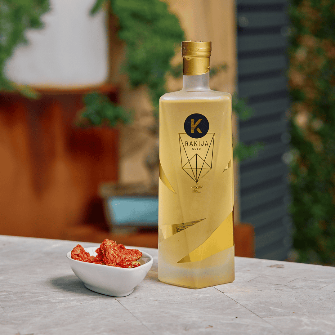 Bottle of Rakija with a small bowl of red snacks on a table outdoors.